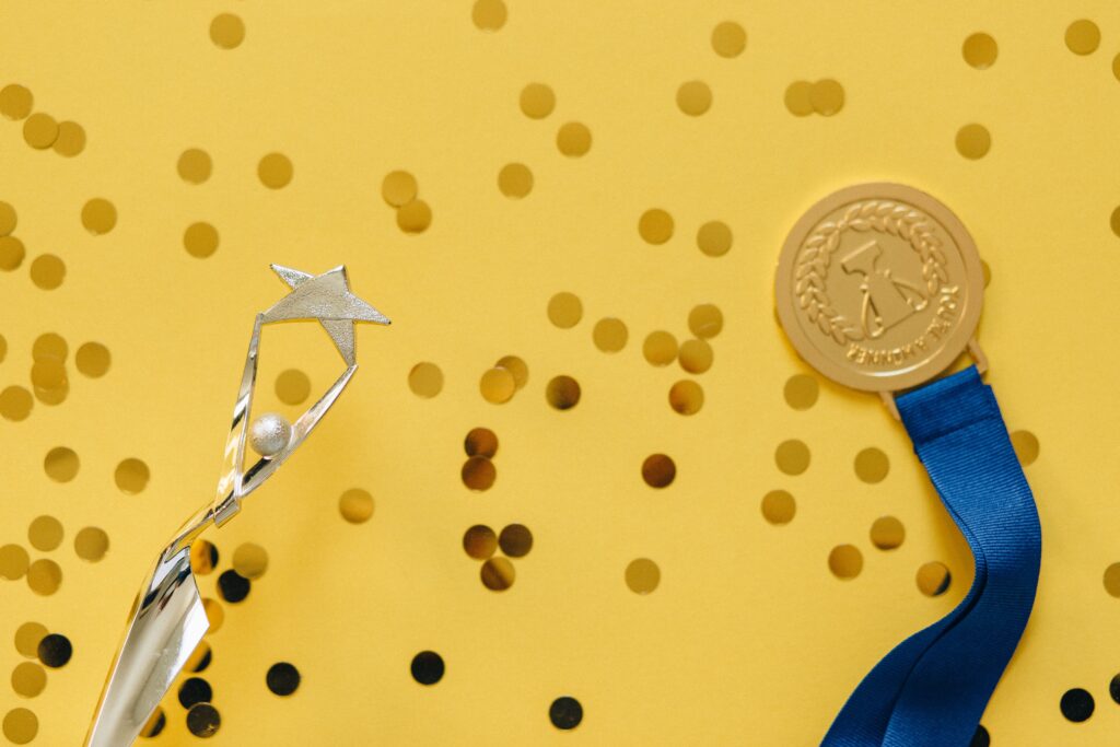 Academics Golden medal and silver trophy with confetti on yellow surface, celebrating achievement.